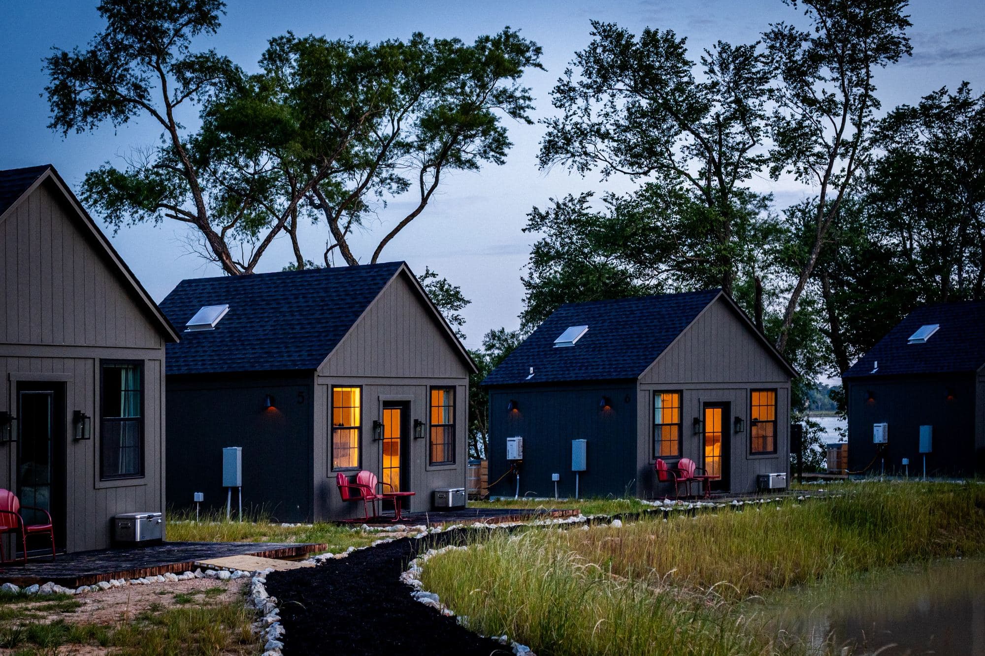 Cabins at dusk with the windows lit, red chairs on each porch