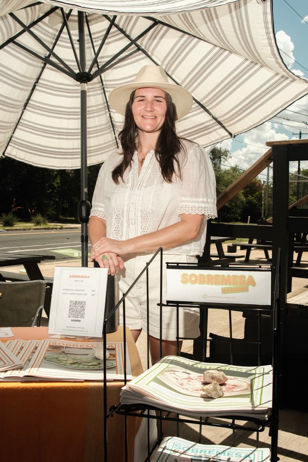 Katie Rice at a Sobremesa Magazine stand, under a striped umbrella
