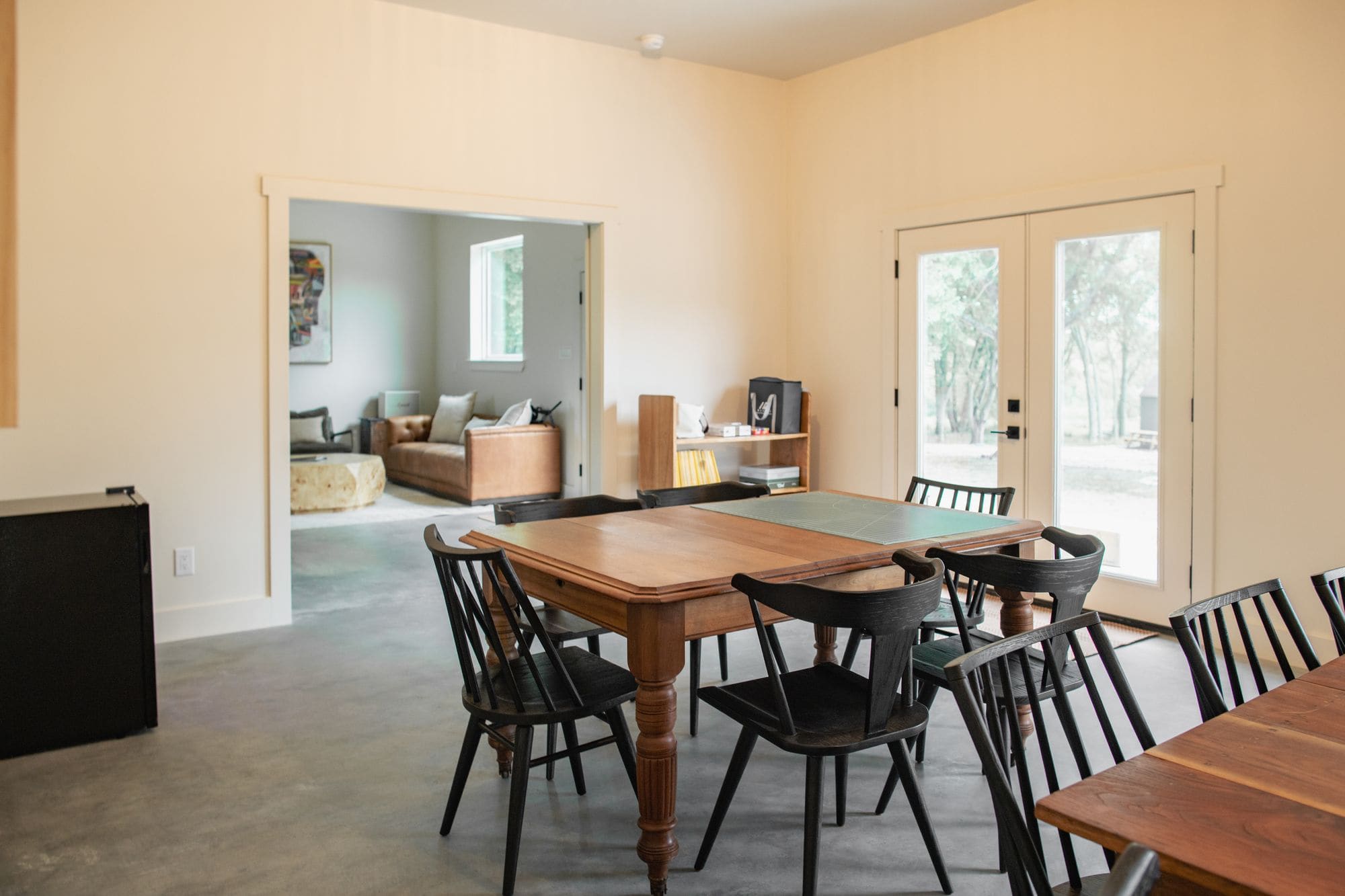 Long wooden dining table with black chairs in the commons barn, with French doors beyond