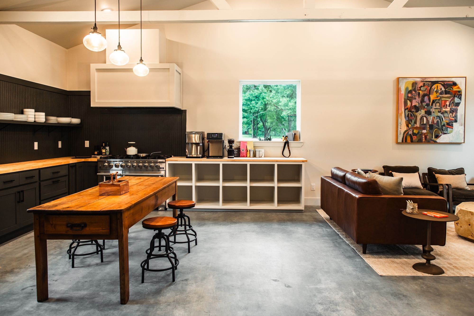 Commons barn kitchen with a six-burner range, a farm table with stools and the lounge beyond