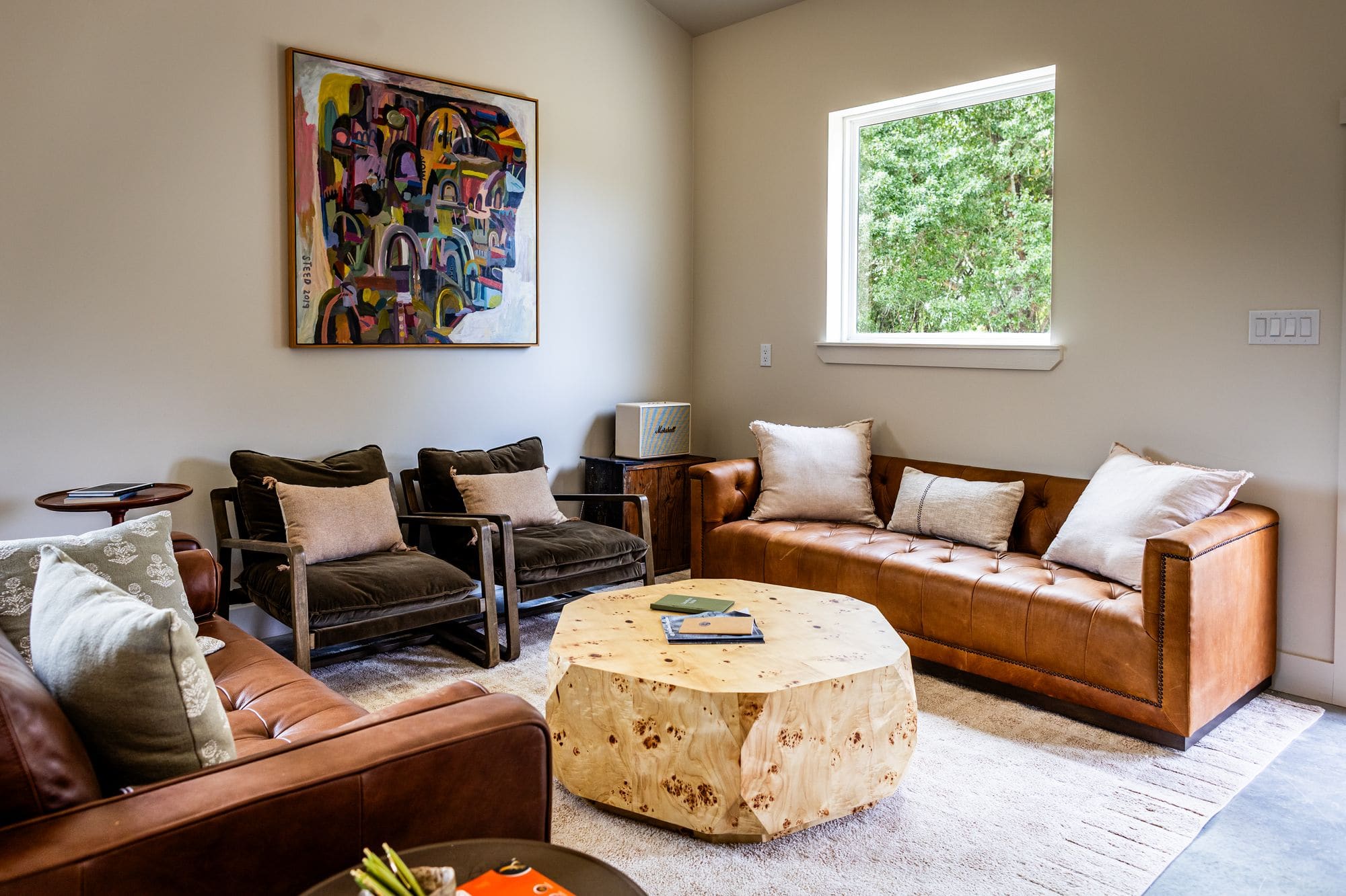 Leather sofas and armchairs around a burl-wood coffee table, with a window to the trees
