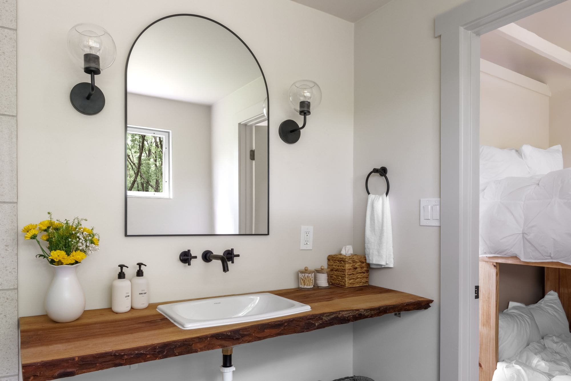 Cabin bathroom with an arched mirror, black fixtures and a live-edge wood vanity with yellow flowers
