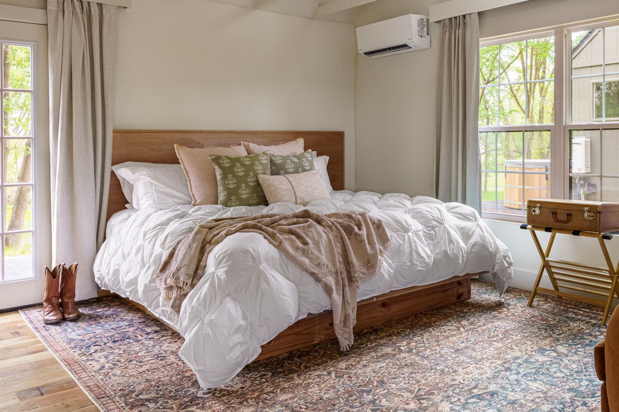 Cabin bedroom with a wood-framed bed, patterned rug, linen curtains and a pair of cowboy boots