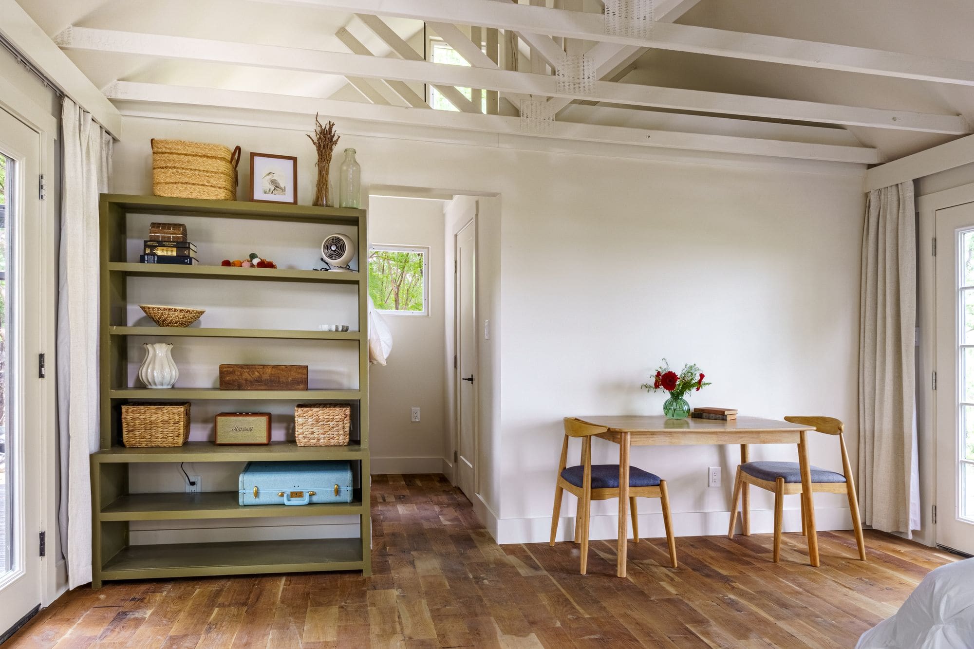 Cabin interior with an olive-green bookshelf, a small table with flowers and a vaulted ceiling