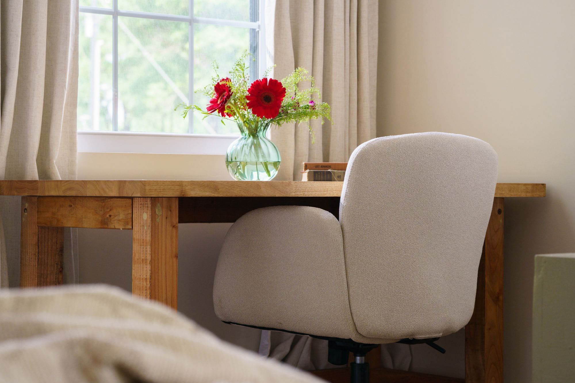 Wooden cabin desk with red flowers in a glass vase and a cushioned chair by the window