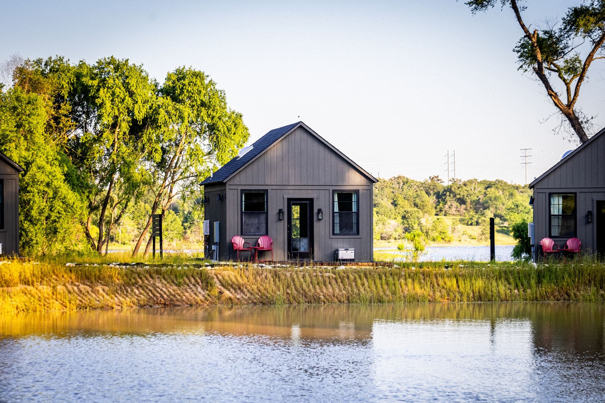 A cabin reflected in the still pond with tall grass and the lake beyond