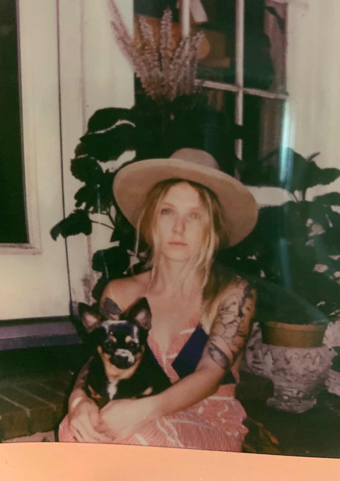 A Polaroid of Hannah Slattery in a wide-brimmed hat, holding a small dog
